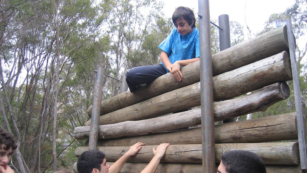 boy climbs over wall of logs obstacle course in Melbourne