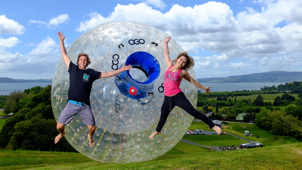 Show item 1 of 4. Zorbing orb with couple jumping on grass, Rotorua New Zealand