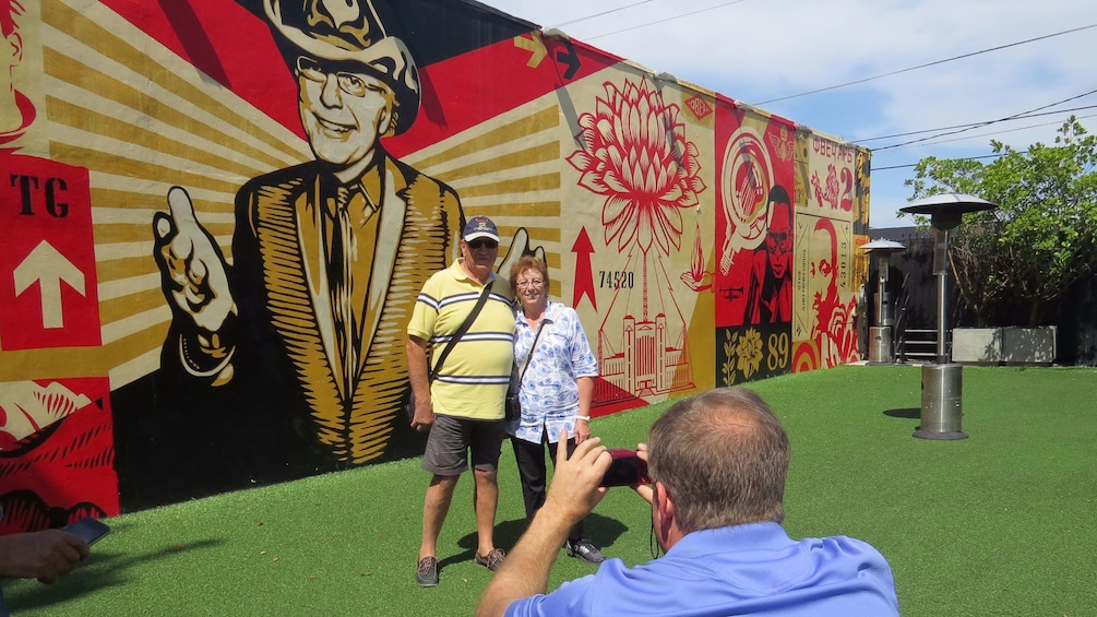 Couple posing for a picture in front of a mural on a buildings side
