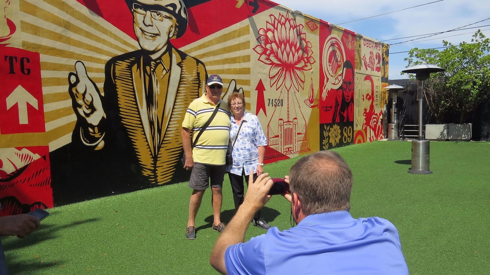 Two people pose for a picture next to a mural