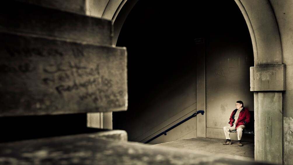 Man in a red jacket sitting behind an archway in Sydney