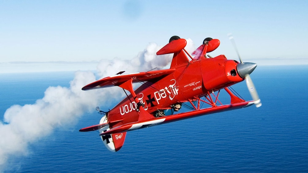 Red Bi-plane leaving smoke trail in the sky in Sydney