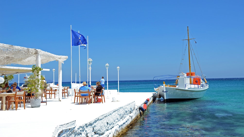 Couple eating lunch at a seaside restaurant with sailboat docked nearby on Mykonos