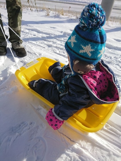 Show item 2 of 5. Small child sits in sled at Yeti Snow Park