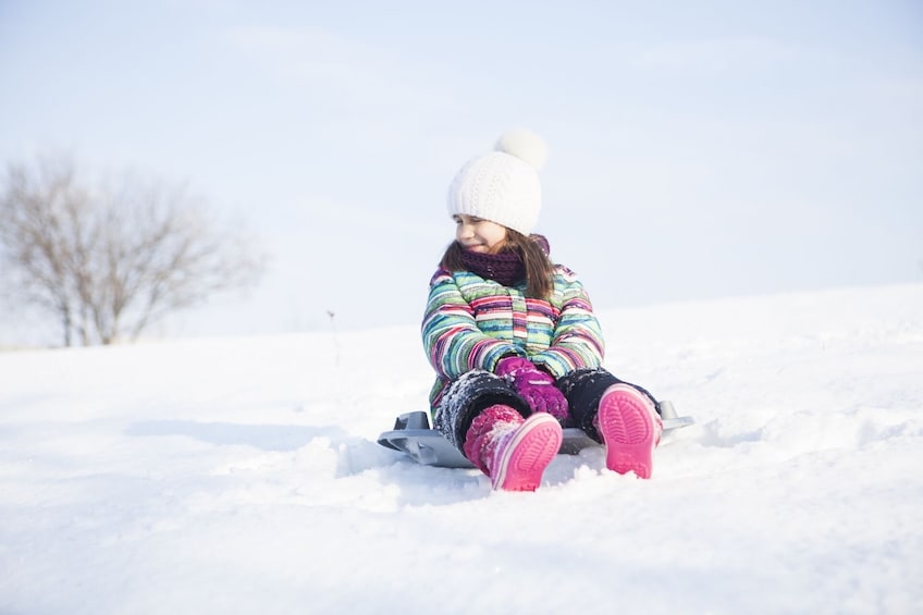 Show item 1 of 5. Little girl sits on round sled in snow at Yeti Snow Park