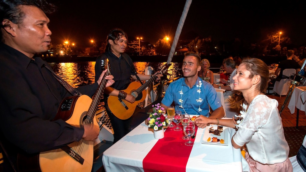 Tampilkan item 4 dari 5. Musicians playing their guitar for a couple on a night cruise in Bali Hai