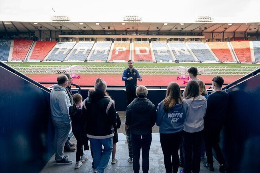 A tour guide shows visitors the pitch and stadium bowl from the trophy presentation area