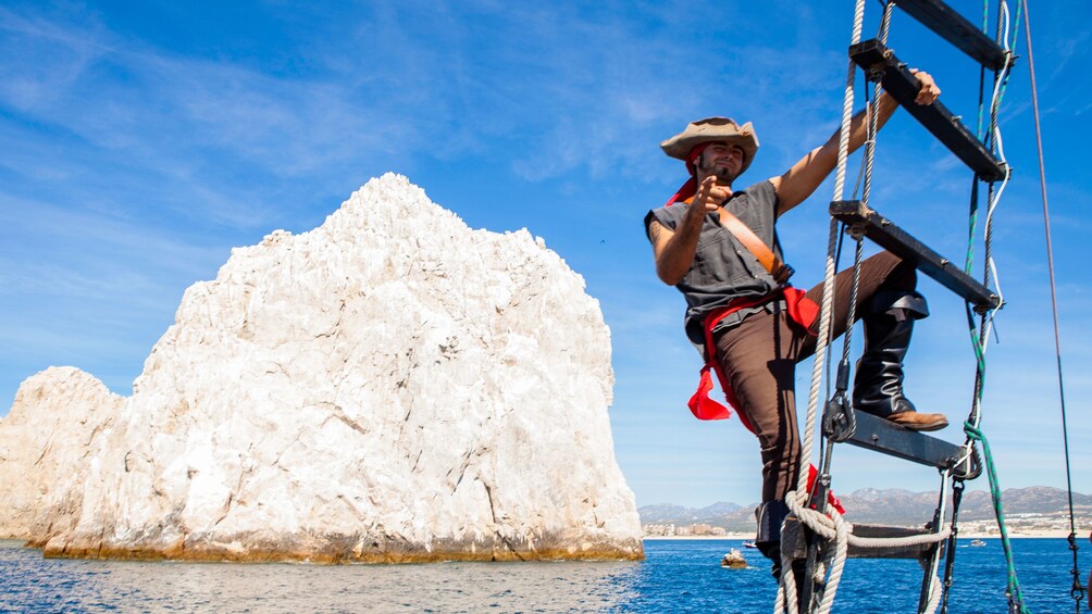 man in pirate costume on ladder in front of sea stack in Los Cabos