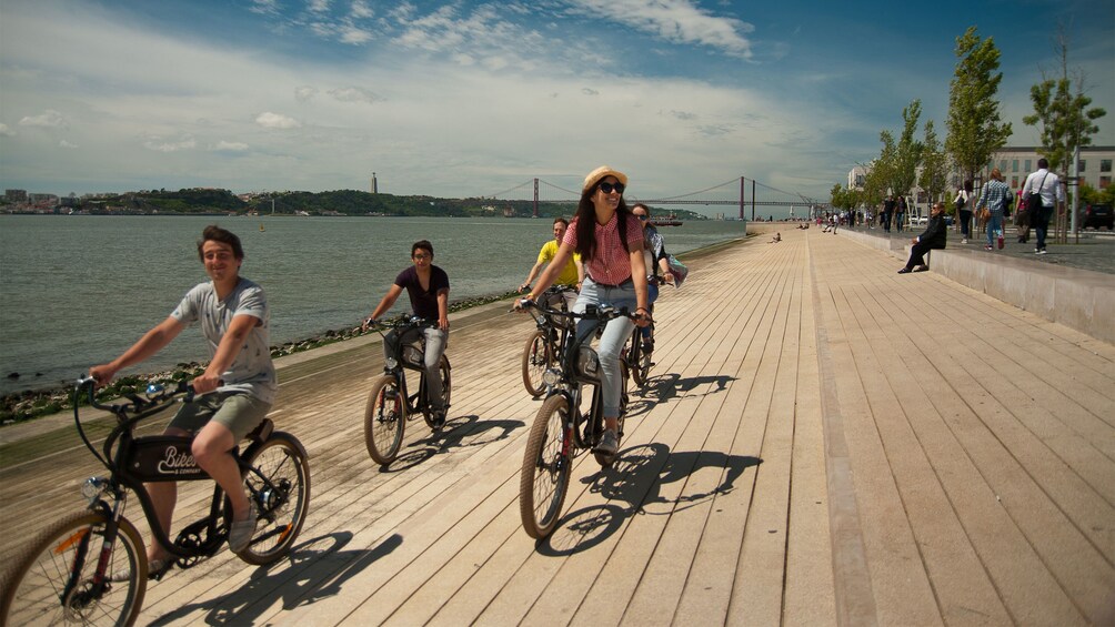Bicycling group riding along the water on the boardwalk in Lisbon