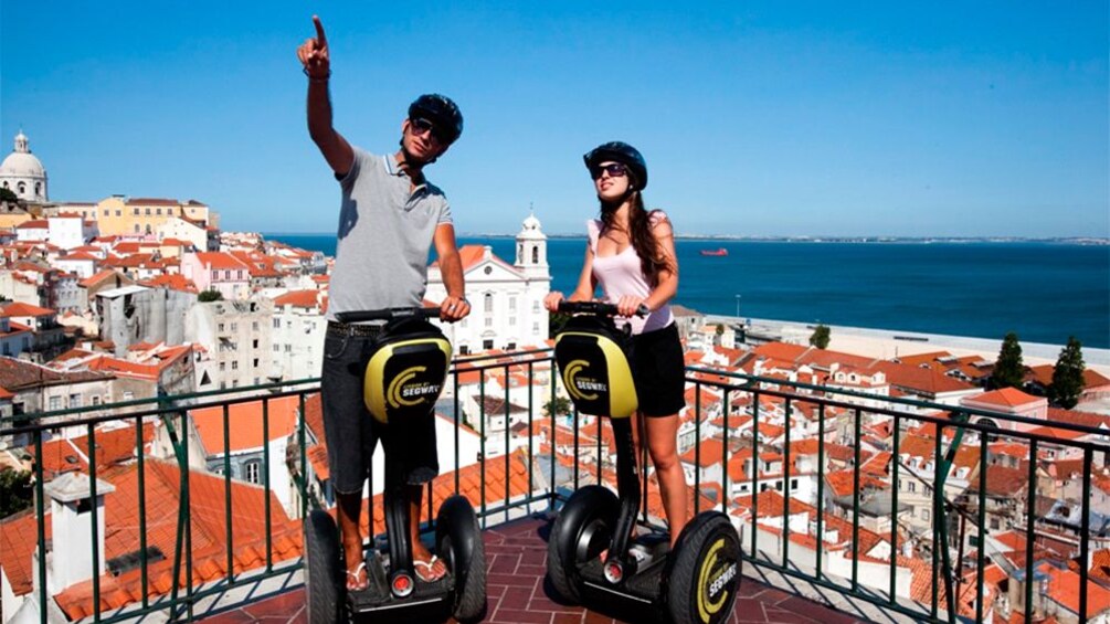 Couple on segways at a scenic viewpoint above the red roofed buildings of Lisbon