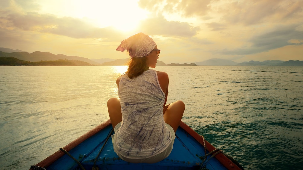 Woman sitting on the bow of a fishing boat at sunset in Pulau Ketam