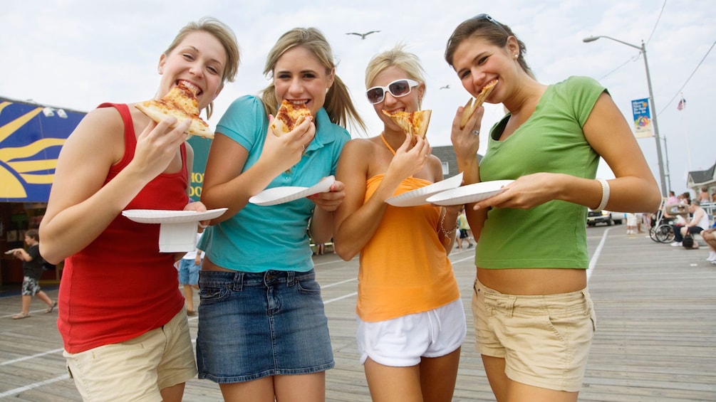 Four women eating pizza on a boardwalk in San Diego