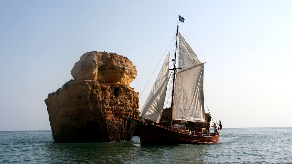 Pirate-themed sailboat alongside a rock formation jutting out of the water off the coast of Algarve