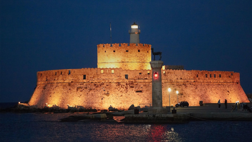 lighthouse and fortress walls lit at night in Rhodes