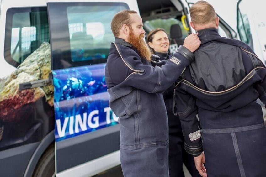 Guide helping a diver getting dressed in a drysuit