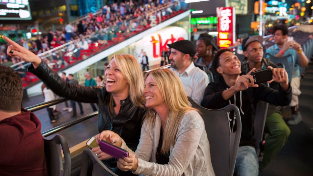 Smiling tourists point at the sights from the top of a double decker bus in New York