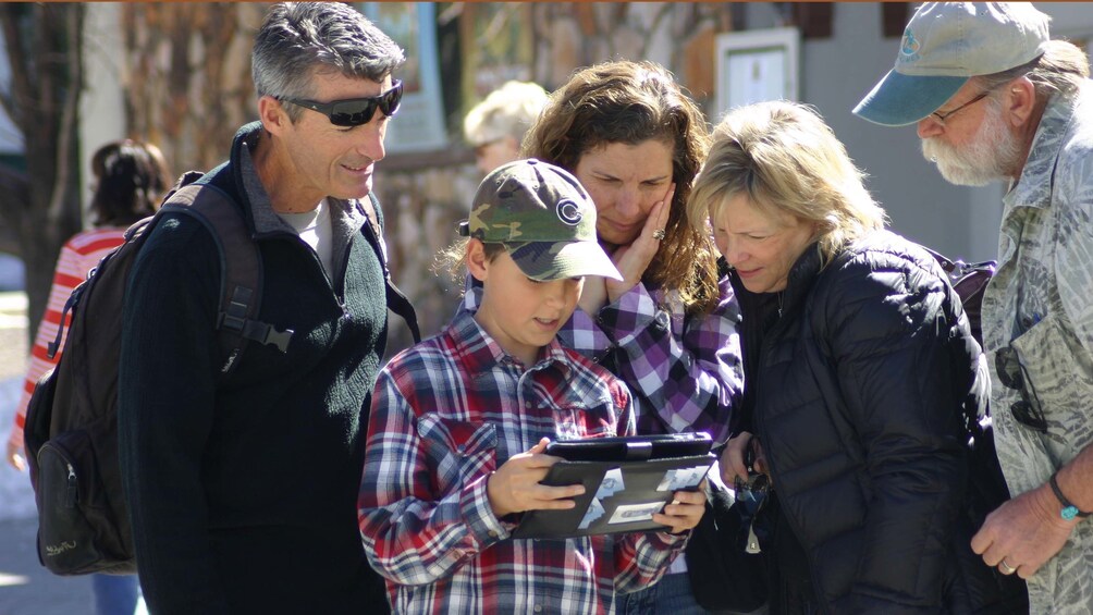 Show item 1 of 5. Multi-generational family looking at handheld device during a family scavenger hunt