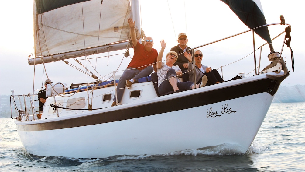 People on bow of sailboat wave as they pass by off San Diego