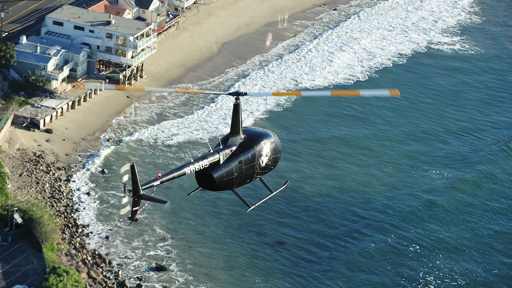 black helicopter soaring along the beachfront in Los Angeles