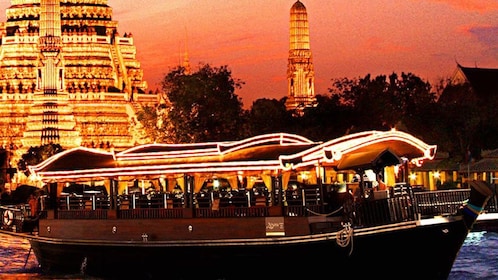 Dinner cruise boat sailing past an illuminated temple at sunset