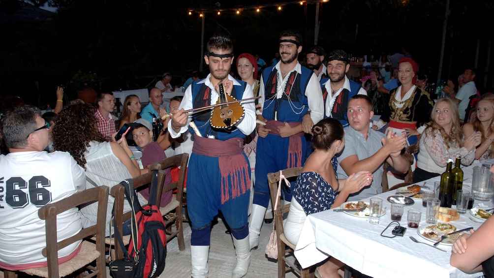 Greek musicians walk past tables of diners in Crete