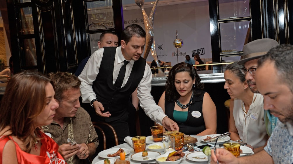 Group at a food tour sitting around a round table as a server is serving food to everyone