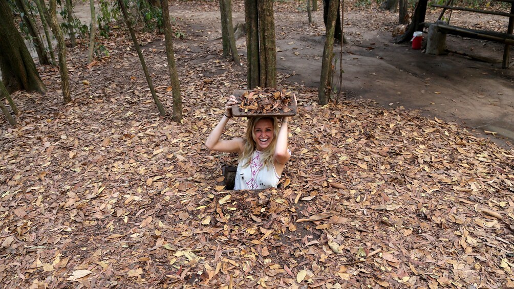 Woman popping out of a tiny tunnel in the ground in Cu Chi
