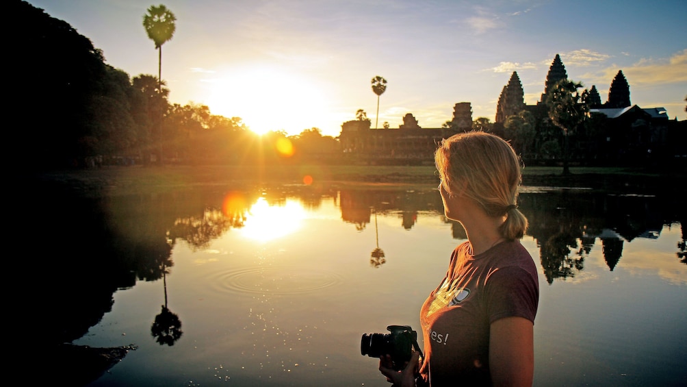 Woman with camera and Angkor Wat in the background at sunset in Siem Reap