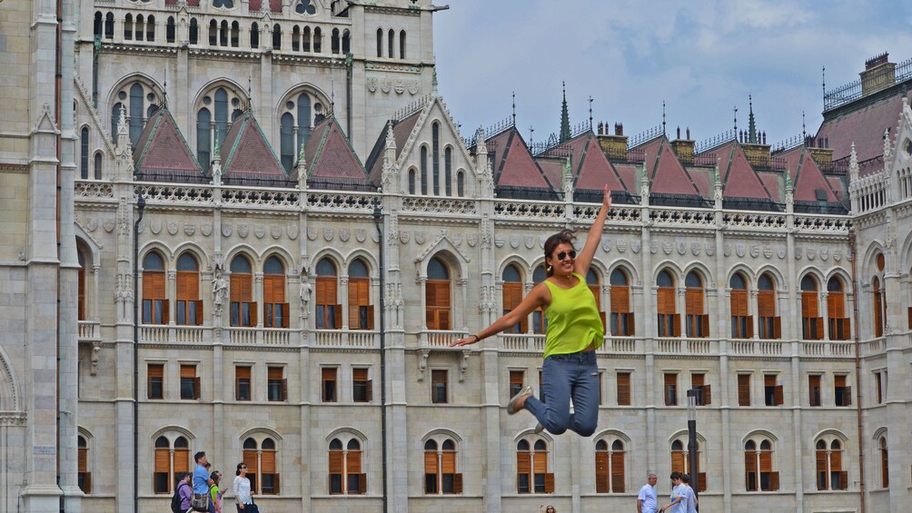 A woman jumping in front of a gothic style building in Budapest