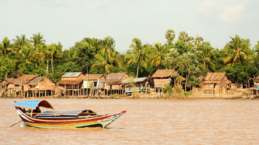 Show item 1 of 8. Boat passing a village along the bank of the Yangon River in Myanmar