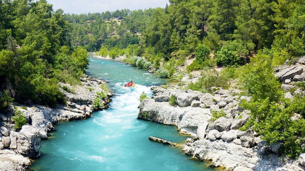 People in a raft making their way down a bright blue river in Antalya