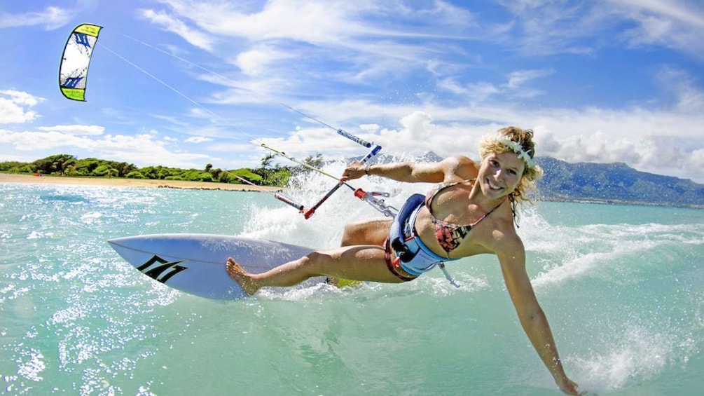 Smiling woman cresting a wave riding a kiteboard