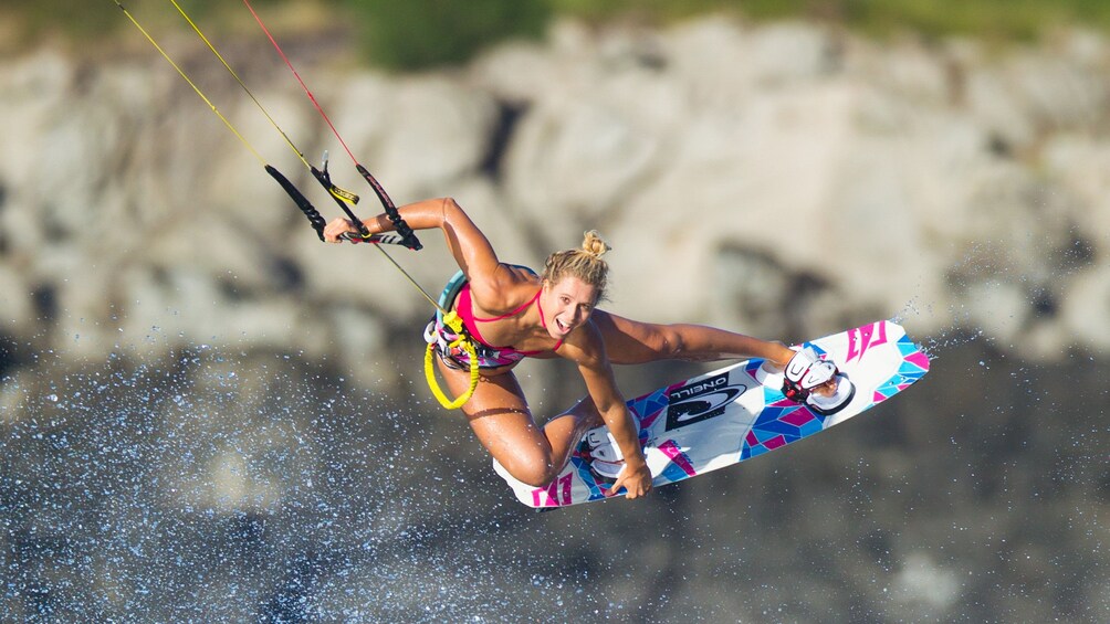 Woman looking at he camera grabs her kiteboard while airborne