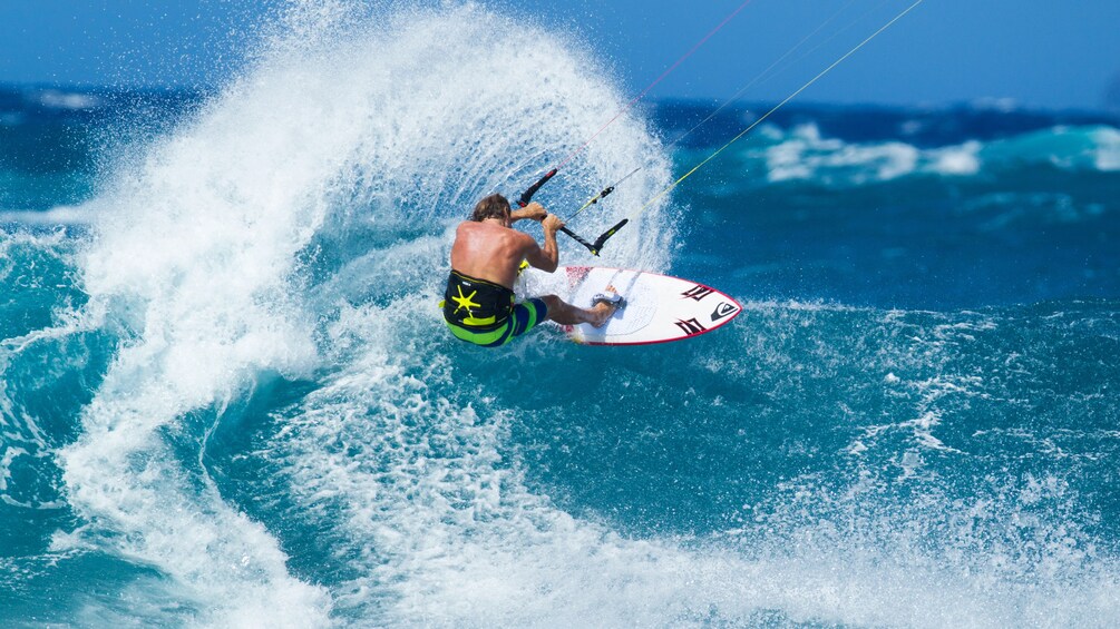 Man rides the waves while holding on to his kiteboard