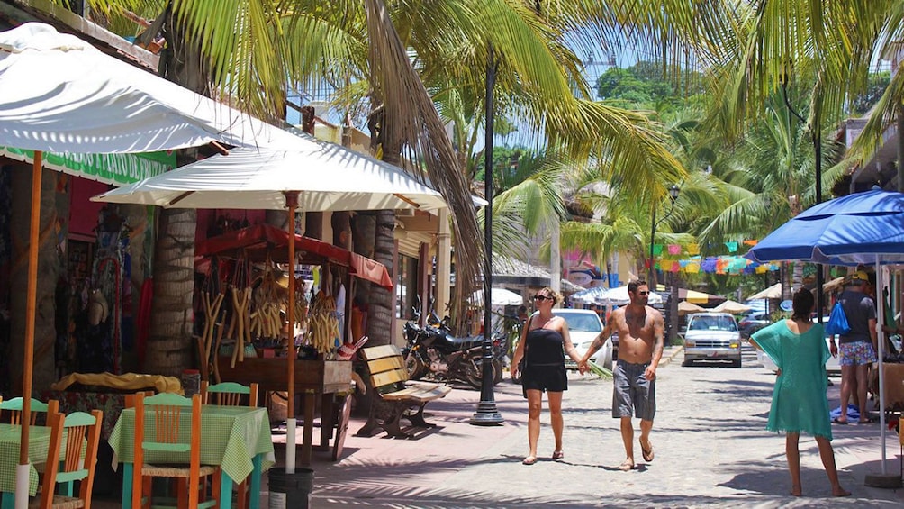 Couple walking past souvenir carts and outside dining in Sayulita