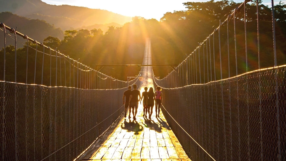 Hiking group heads over bridge towards setting sun