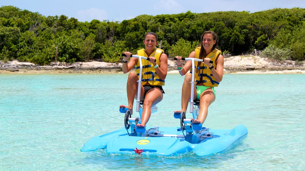 Two women ride a pedal-powered raft on the water in the Bahamas