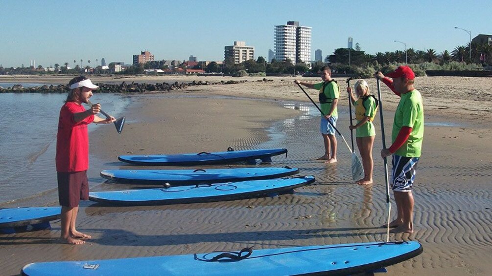 Instructor coaches group of students about paddle boarding