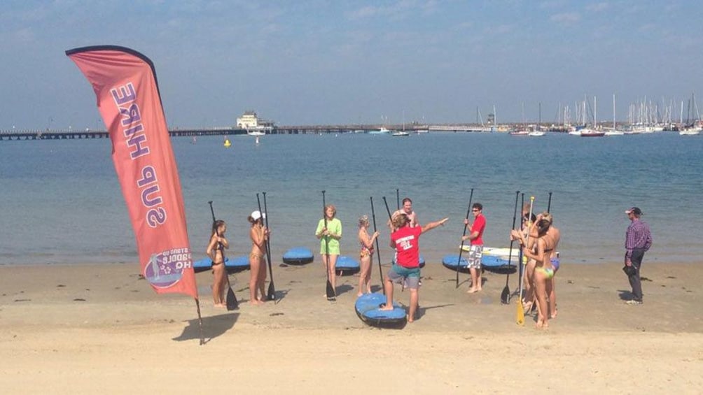 Students stand next to Paddle Board sign with paddles in hand