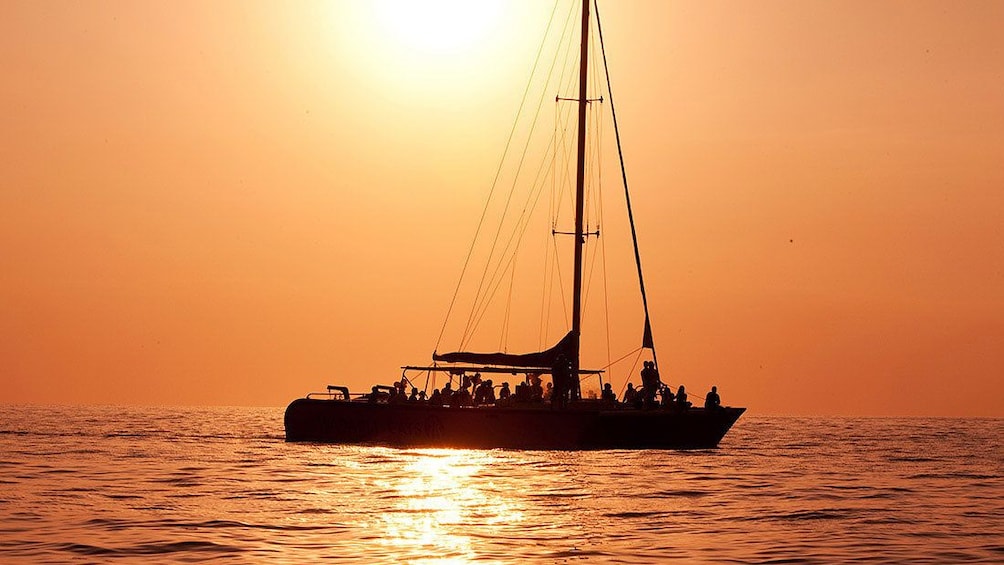 Silhouette of sail boat filled with people at sunset.