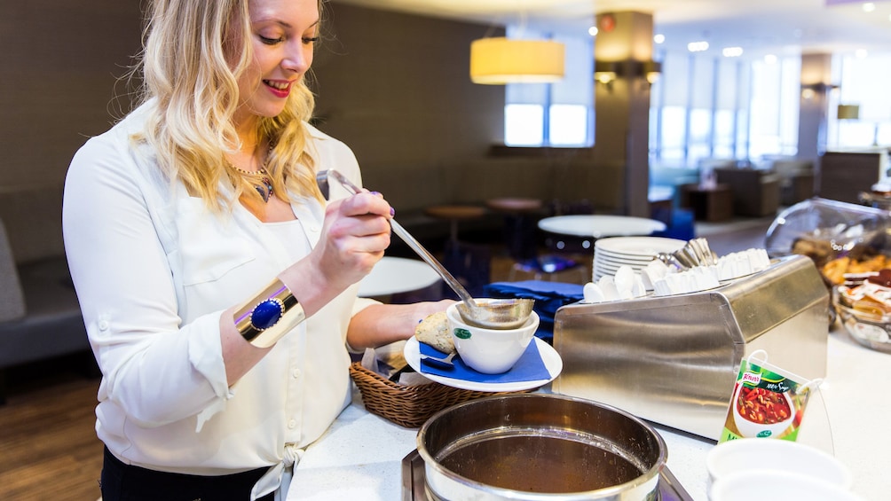 woman helping herself to complimentary soup inside the Aspire airport Lounge