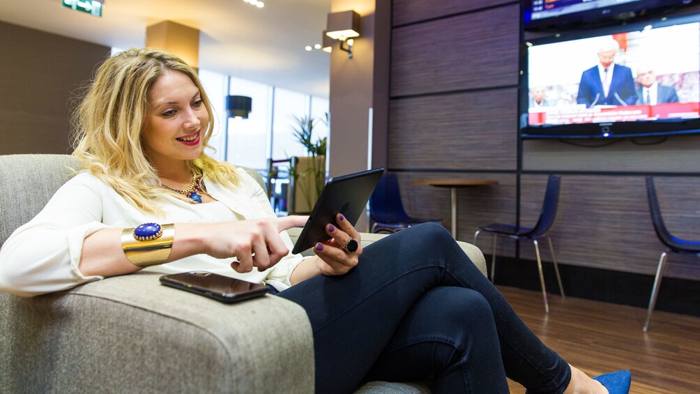 Show item 2 of 5. woman reading her tablet device at the airport lounge