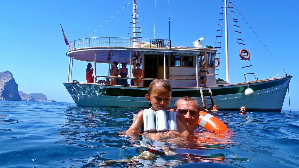 Father and daughter swim next to anchored boat in Pollensa Bay