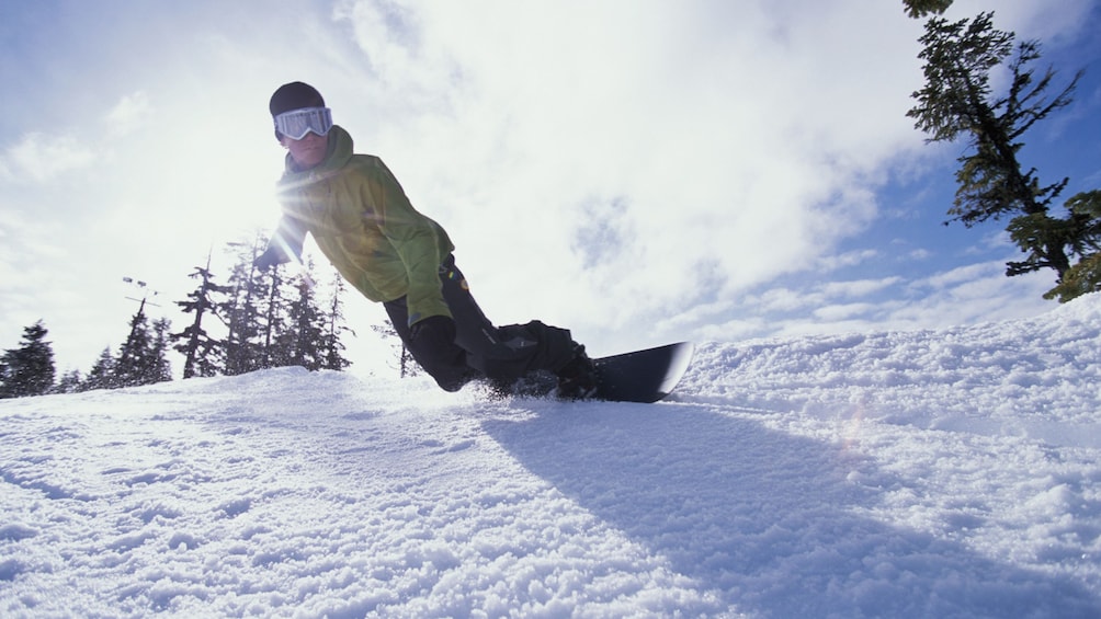 Foto 1 van 5. Snowboarder gliding down a slope on a bright afternoon