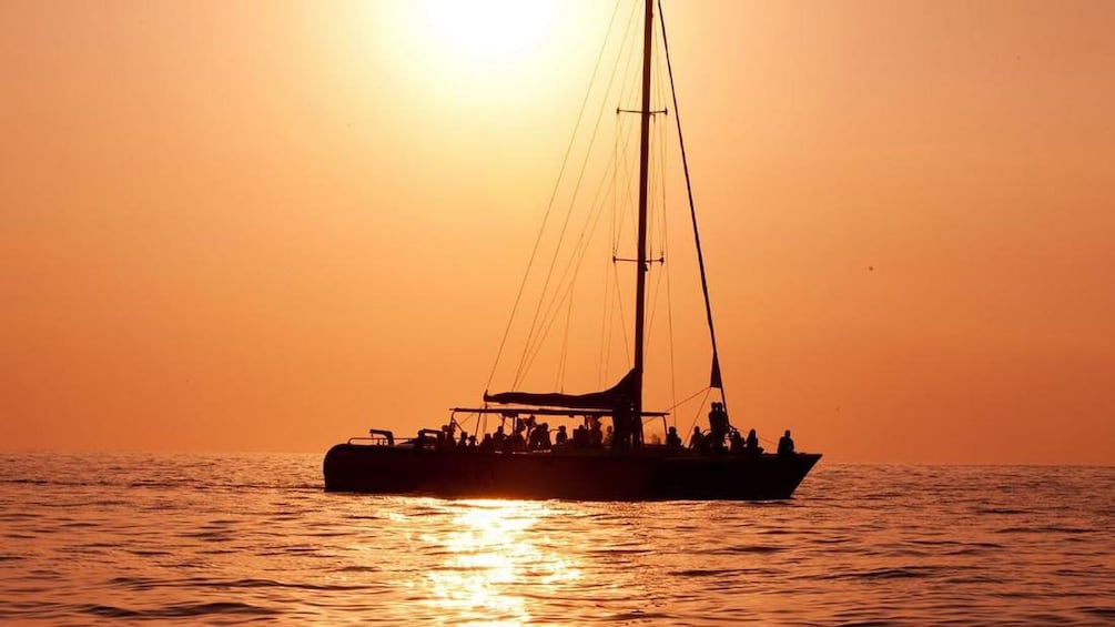 Silhouette of sailboat with several passengers aboard at sunset.