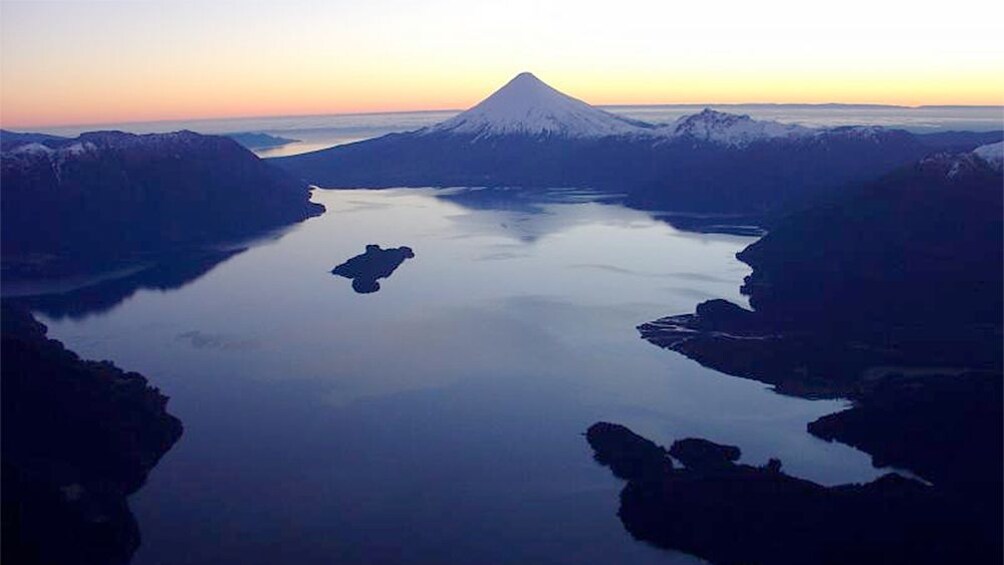 Aerial view of lake with volcano in the distance at sunset.