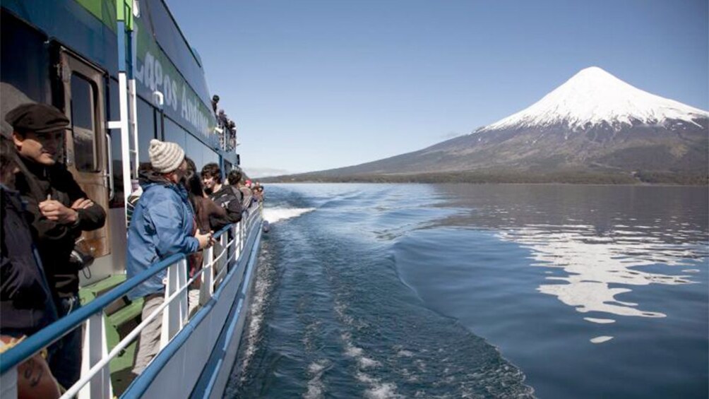 Tourists on ferry boat observing large volcano in the distance.