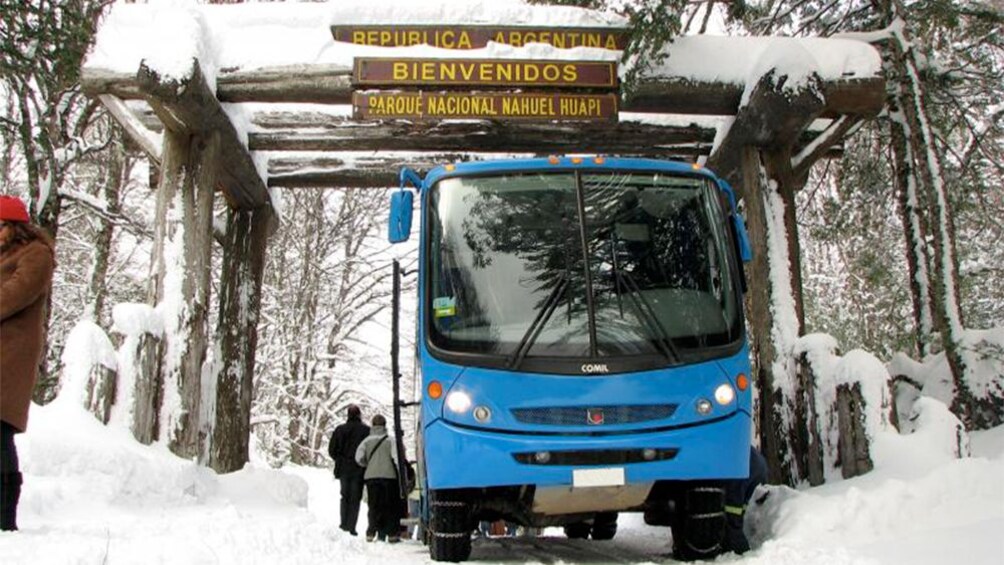 Bus parked under welcome sign in snowy area.