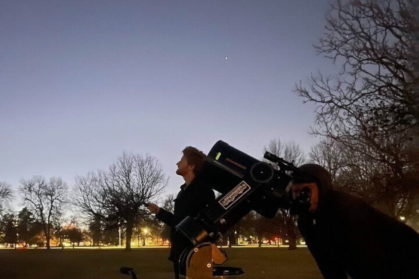 An astronomer guides a guest at AstroTours.ors's Mile High Night Sky program set up at city park