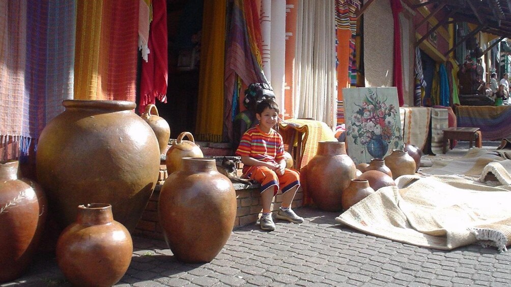 Young boy at a craft store selling colorful textiles and large pots in Sao Paulo